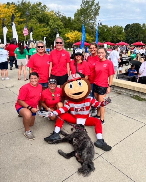 Elizabeth "Biz" Them poses with OSU's Brutus the Buckeye along with six other people all dressed in red