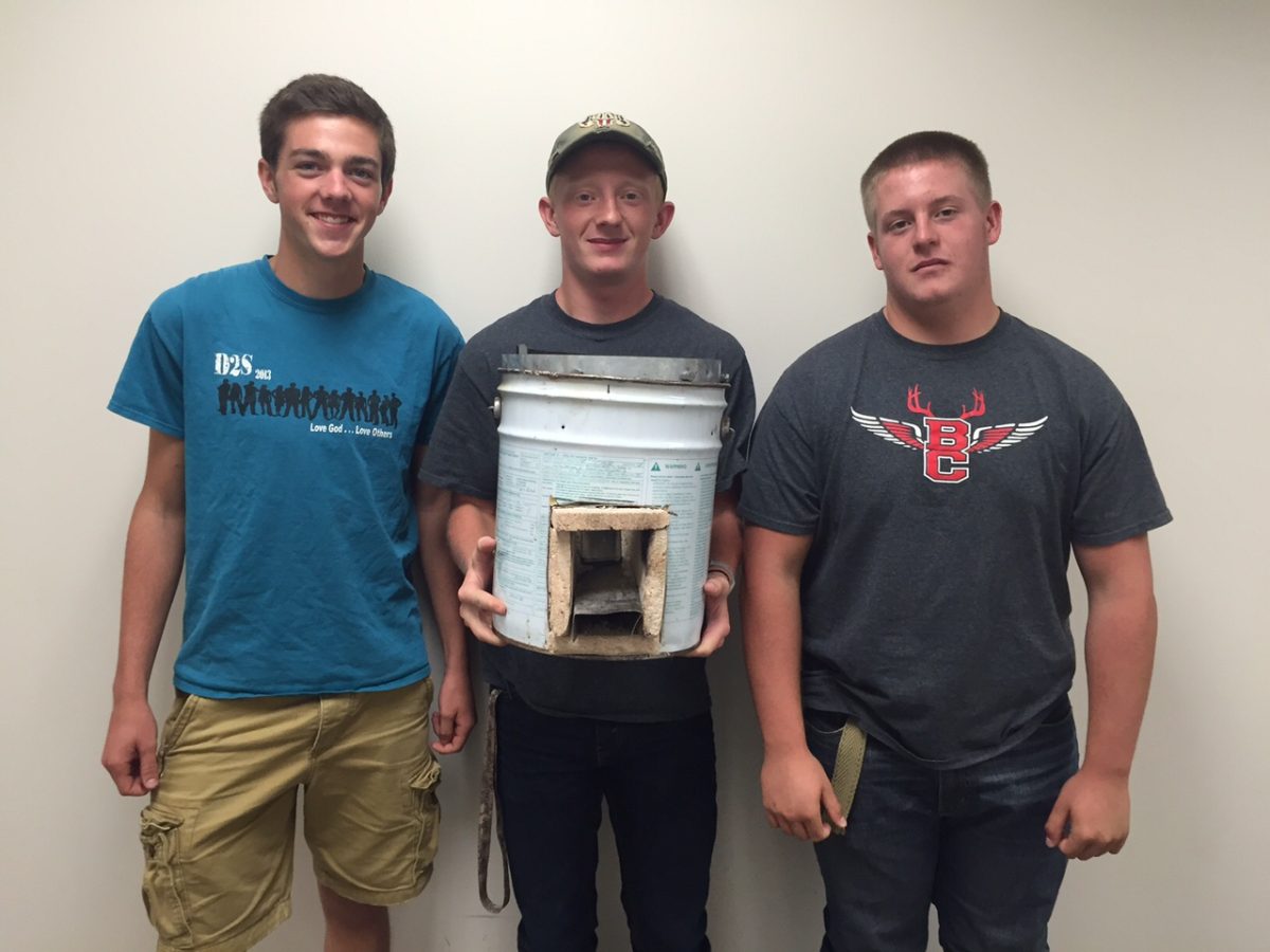 Three students hold a rocket stove they made
