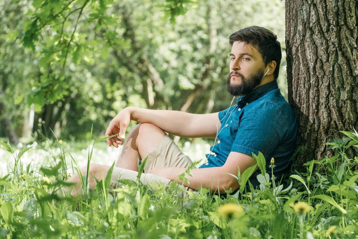 Young man leaning against a tree listening to music.