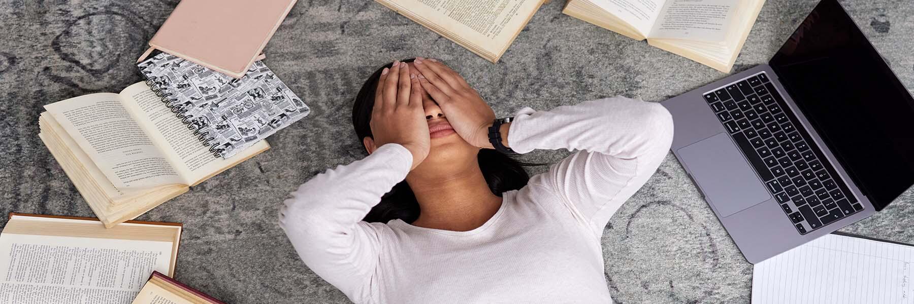 Stressed woman laying on the floor surrounded by books