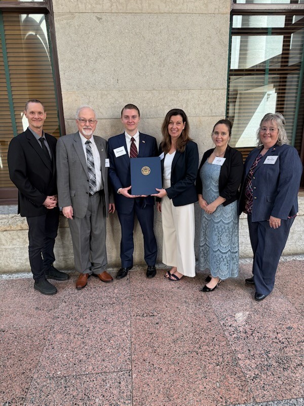 Jesse Halfhill holds in award surrounded by his family, college representatives, and state representatives.