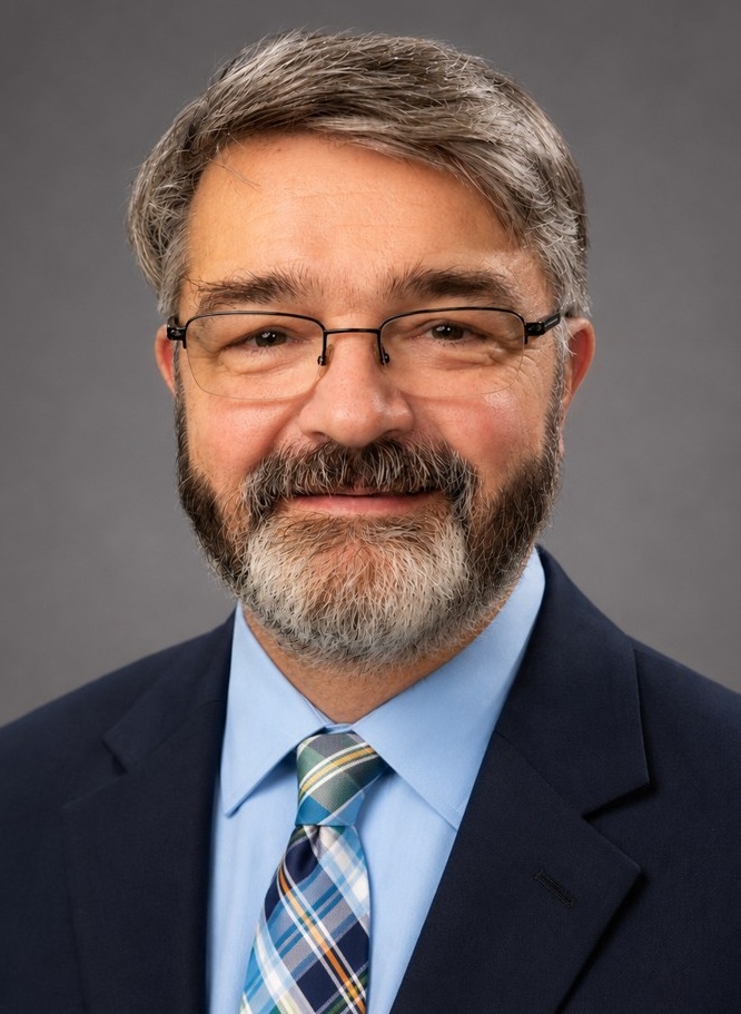 Man with blue shirt and tie wearing glasses and smiling